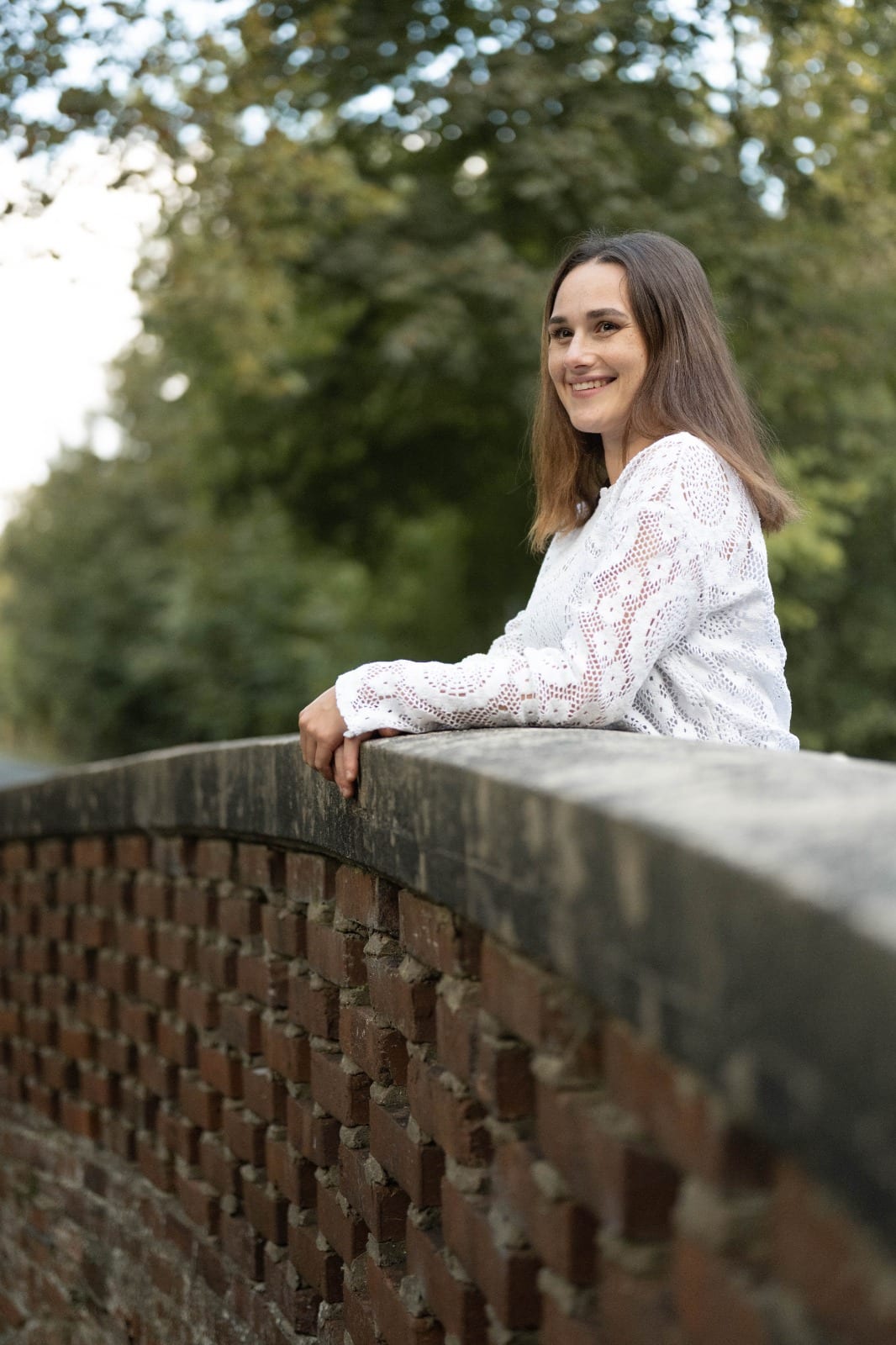 Junge Frau stützt sich auf eine Backsteinbrücke und lächelt über die Schulter