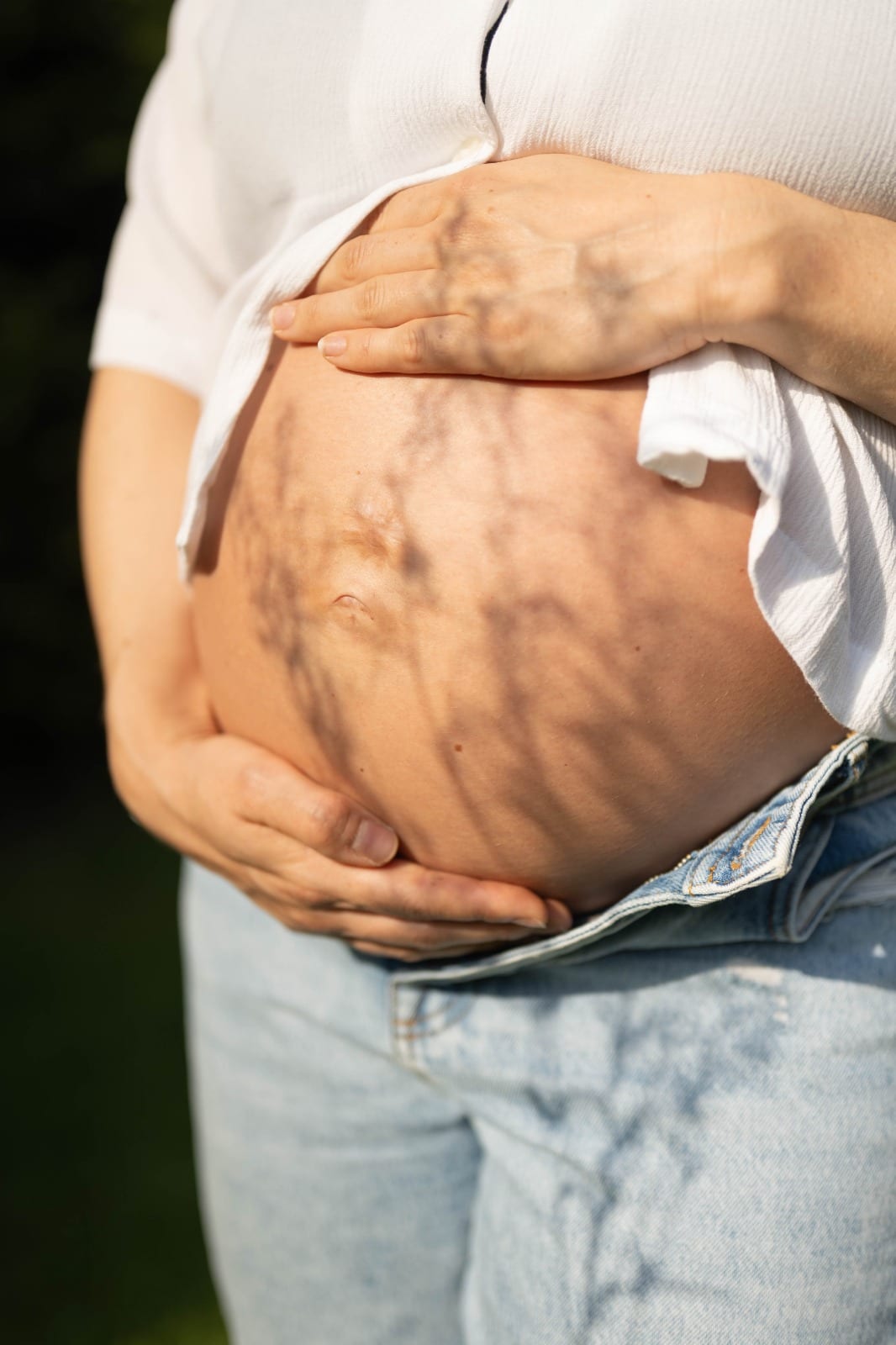 Schwangere hält ihren Babybauch mit Schattenspiel im Sonnenlicht